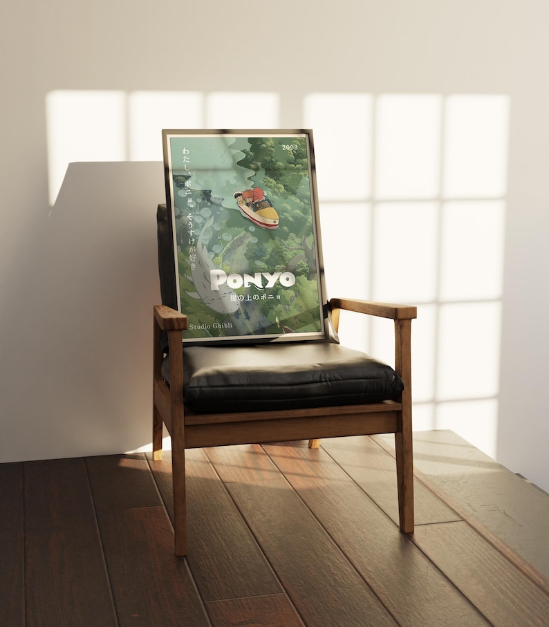 May include: A framed poster of the animated film "Ponyo" by Studio Ghibli, leaning against a black leather chair. The poster features a colorful illustration of a boat and the film's title in white. The chair has a wooden frame.