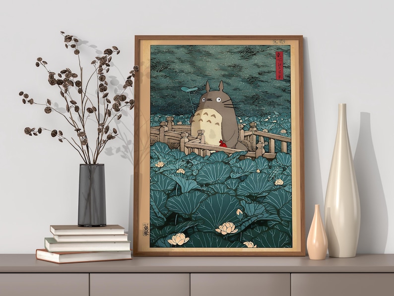 May include: Framed art print depicting a large, grey, furry creature on a wooden bridge, surrounded by lily pads. The artwork has a Japanese aesthetic with a muted colour palette of greens, blues, and browns. The frame is a warm brown colour.