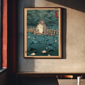 May include: A framed print depicting a scene with a large, grey Totoro character on a wooden bridge, surrounded by large lily pads and lotus flowers. The artwork has a traditional Japanese aesthetic with a muted colour palette.