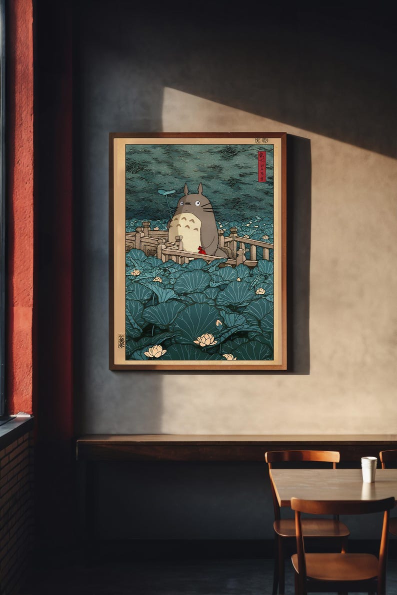 May include: A framed print depicting a scene with a large, grey Totoro character on a wooden bridge, surrounded by large lily pads and lotus flowers. The artwork has a traditional Japanese aesthetic with a muted colour palette.