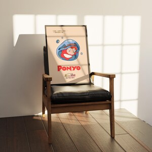 Puede incluir: Un p&oacute;ster enmarcado con el personaje animado Ponyo, con el t&iacute;tulo en rojo. La imagen muestra a Ponyo en una burbuja azul. El p&oacute;ster est&aacute; apoyado en una silla de cuero negro con brazos y patas de madera.