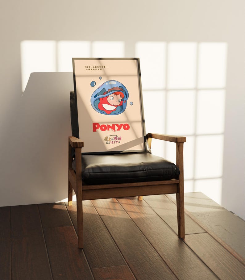 Puede incluir: Un p&oacute;ster enmarcado con el personaje animado Ponyo, con el t&iacute;tulo en rojo. La imagen muestra a Ponyo en una burbuja azul. El p&oacute;ster est&aacute; apoyado en una silla de cuero negro con brazos y patas de madera.