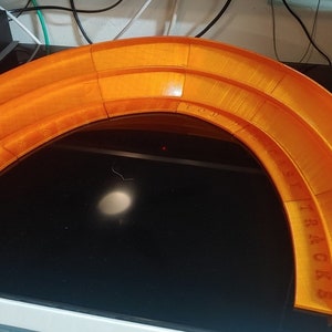 Könnte beinhalten: Orangenes Plastik-Rennspielzeug für Spielzeugautos. Die Rennbahn ist gebogen und hat drei Spuren. Die Rennbahn ist mit "Track Set" beschriftet.