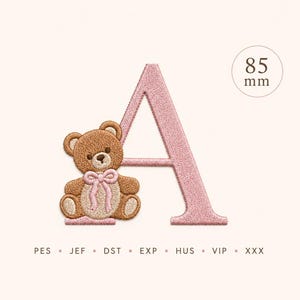 Puede incluir: Una letra A bordada en hilo rosa claro, acompañada de un oso de peluche marrón con un lazo rosa claro alrededor del cuello. El diseño mide 85 mm de altura. Debajo del diseño, el texto dice PES, JEF, DST, EXP, HUS, VIP, XXX.