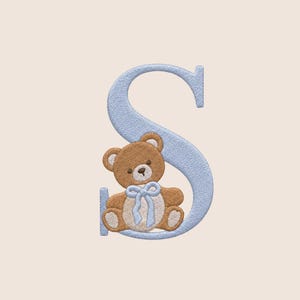 May include: A light blue embroidered letter S featuring a textured finish. A brown teddy bear with a cream-colored belly and muzzle is positioned in front of the letter, wearing a light blue ribbon tied in a bow around its neck.
