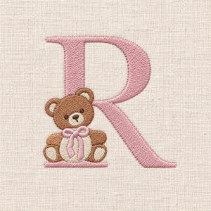 以下が含まれることがあります： 淡いピンク色の糸で刺繍された文字「R」と、その足元に座る茶色のテディベア。テディベアはクリーム色の腹部を持ち、首にはピンクのリボンが結ばれており、すべて明るいベージュ色の布地に刺繍されています。