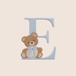 May include: An embroidered capital letter E in light blue thread featuring a brown teddy bear sitting at the base. The bear has a cream-coloured belly, a dark brown nose, and a light blue ribbon tied in a bow around its neck, all in embroidery.