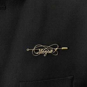 May include: Gold wire lapel pin with the name "Megan" written in cursive.