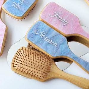 May include: Set of four wooden hair brushes with a light blue and pink marbled design. Each brush has a different word spelled out in rhinestones: "Bride", "Maid of Honor", "Matron of Honor", and "Bridesmaid".
