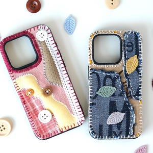 May include: Two smartphone cases featuring fabric patchwork designs. The left case has pink, yellow, and plaid fabric with white lace and buttons. The right case features blue denim with printed text, beige fabric, and small embroidered leaf appliqués.