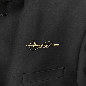 May include: A gold-colored pin with the word "Brenda" written in cursive.