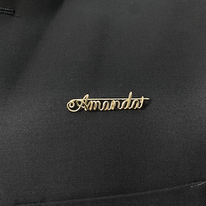 May include: Gold wire name pin with the name "Amanda" spelled out.