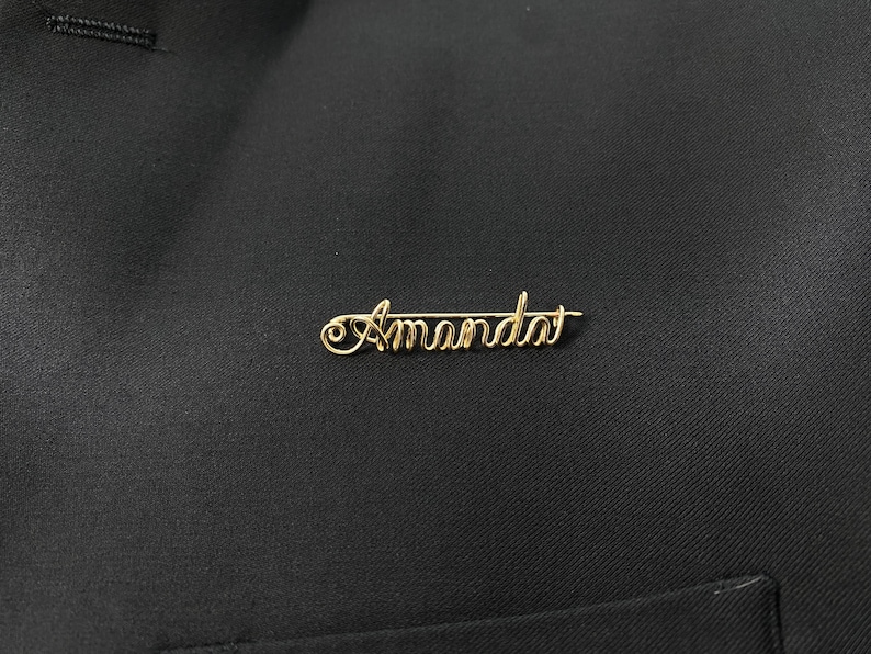 May include: Gold wire name pin with the name "Amanda" spelled out.
