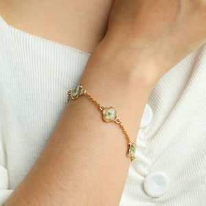 May include: A gold chain bracelet with four clover-shaped charms, each containing a pressed white flower.