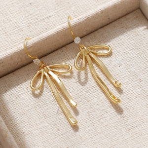 May include: A pair of gold-tone dangle earrings with a bow design and a small clear crystal accent.