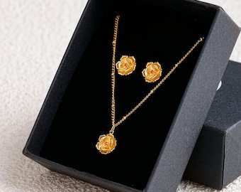 Peut inclure: Un ensemble collier et boucles d'oreilles en or avec un motif de fleur. La fleur a un centre rouge et des pétales jaunes.