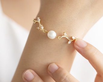 May include: A gold bracelet with a delicate vine design and a single pearl charm. The bracelet is adorned with small clear crystals.