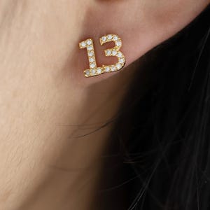 May include: Gold-tone number thirteen earring with clear cubic zirconia stones.