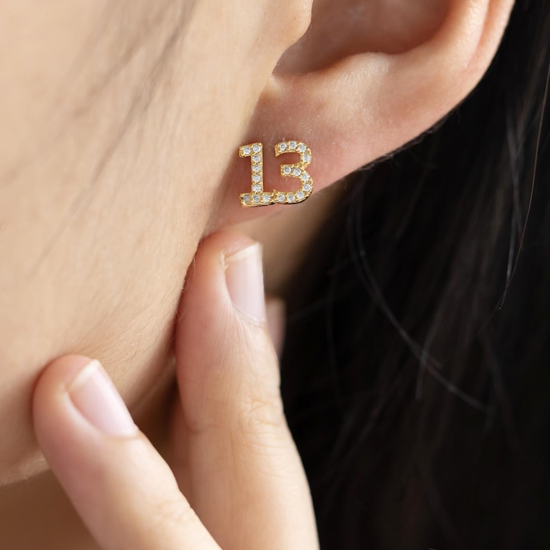 May include: Gold earrings with a number 13 design, outlined with small clear stones.
