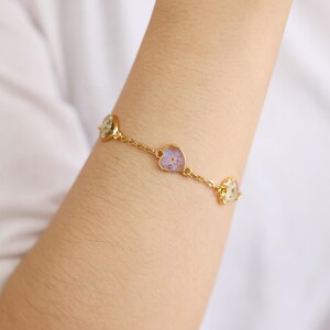Op de afbeelding: Een gouden kettingarmband met vier hartvormige bedels. Elke bedel heeft een ander gedroogd bloemenmotief.