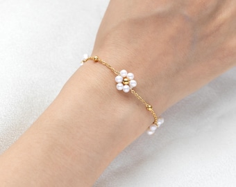 May include: A gold chain bracelet with small white pearl beads and a flower charm made of pearls.