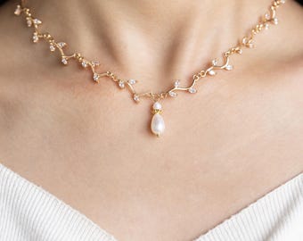May include: A delicate gold necklace with a pearlescent drop pendant. The necklace features a vine-like design with small clear stones.