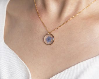 May include: A gold chain necklace with a round pendant featuring a pressed blue flower encased in clear resin.