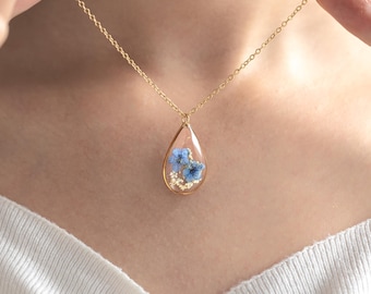 May include: A gold chain necklace with a teardrop-shaped pendant containing pressed blue flowers.