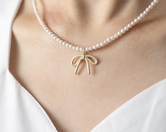 May include: A delicate pearl necklace with a gold bow pendant. The necklace is white and the bow is a simple, elegant design.