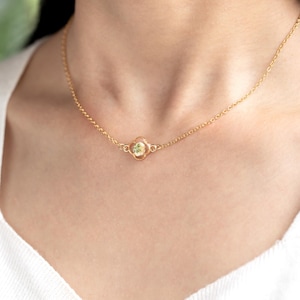 May include: A gold chain necklace with a small, round pendant featuring a pressed flower in a clear resin setting.