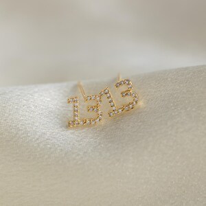 May include: A pair of gold earrings with the number "13" set with small clear stones.