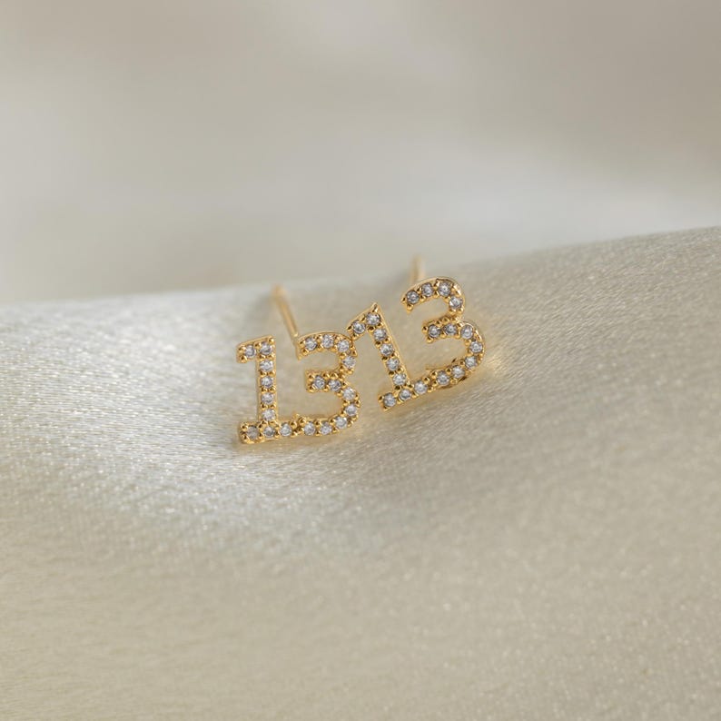 May include: A pair of gold earrings with the number "13" set with small clear stones.