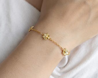Puede incluir: Un brazalete de cadena dorada con pequeños abalorios con forma de flor. Cada abalorio con forma de flor tiene una pequeña piedra transparente en el centro.