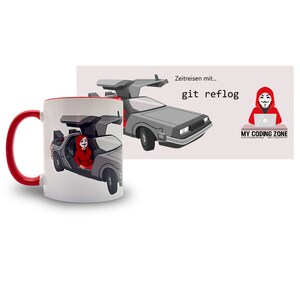 Könnte beinhalten: Weißer Keramikbecher mit rotem Innenraum und Griff. Der Becher zeigt eine Grafik eines DeLorean-Autos mit einer Person in einem roten Kapuzenkostüm. Der Becher hat auch den Text "Zeitresen mit... git reflog" und ein Logo.