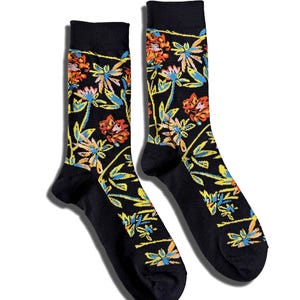 May include: A pair of black crew socks featuring a vibrant floral pattern with stylised flowers in shades of orange, yellow, and light blue. The design covers the leg and foot area of the socks, which have solid black cuffs, heels, and toe sections.
