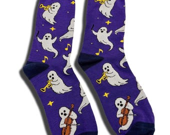 May include: A pair of purple crew socks featuring a repeating pattern of white ghosts playing musical instruments, including trumpets and cellos, interspersed with yellow stars and musical notes. The socks have dark purple cuffs and dark blue toes.