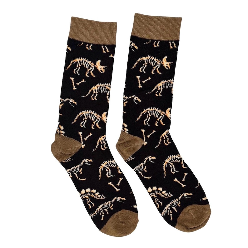 May include: A pair of black socks with a repeating pattern of dinosaur skeletons in tan. The socks have brown heels and toes, and brown bands at the top.