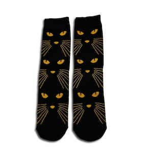 May include: Black socks featuring a repeating pattern of a cat's face. The cat faces have yellow eyes and whiskers. The socks are made of a soft material, suitable for everyday wear.