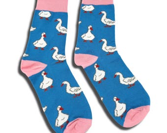 May include: A pair of blue crew socks featuring a repeating pattern of white geese with orange beaks and feet. The socks have solid pink cuffs, heels, and toes, providing a distinct contrast to the blue background and the white goose illustrations.