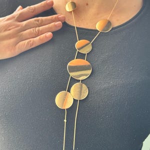 May include: A gold necklace with five round pendant charms. The charms are of different sizes and have a textured finish.