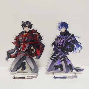 May include: Two acrylic standees featuring anime-style characters. One character wears a black and red outfit, the other a purple and black outfit. Both are kneeling on clear bases with text. The standees are on a white background.