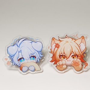 May include: Two clear acrylic pins featuring anime-style characters. One pin depicts a light blue character with a sad expression, while the other shows an orange-haired character with an angry expression. Both pins have a wavy outline.