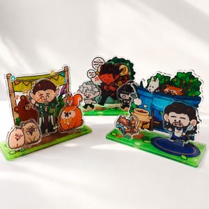 Peut inclure: Trois pr&eacute;sentoirs en acrylique transparent orn&eacute;s d'illustrations de dessins anim&eacute;s color&eacute;s repr&eacute;sentant des personnages fantastiques, des animaux et des sc&egrave;nes foresti&egrave;res. Chaque socle vert pr&eacute;sente des motifs d'herbe et de fleurs.