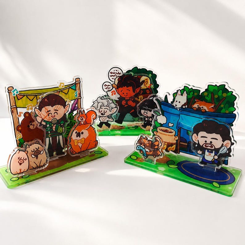 Peut inclure: Trois pr&eacute;sentoirs en acrylique transparent orn&eacute;s d'illustrations de dessins anim&eacute;s color&eacute;s repr&eacute;sentant des personnages fantastiques, des animaux et des sc&egrave;nes foresti&egrave;res. Chaque socle vert pr&eacute;sente des motifs d'herbe et de fleurs.