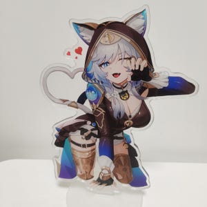 Puede incluir: Un expositor acrílico transparente con un personaje de dibujos animados con cabello blanco, ojos azules y un atuendo con capucha marrón con orejas de gato. El personaje guiña un ojo y hace el signo de la paz. Un diseño en forma de corazón está adjunto.