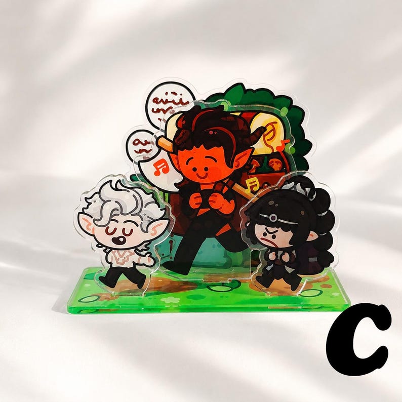 Peut inclure: Un pr&eacute;sentoir en acrylique multicouche repr&eacute;sentant trois personnages de dessin anim&eacute; sur une base verte. Un personnage central &agrave; la peau rouge avec des cornes porte un coffre, flanqu&eacute; d'un personnage aux cheveux blancs et d'un autre aux cheveux noirs.
