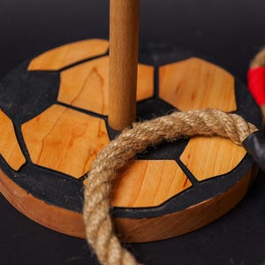 Op de afbeelding: Houten ringwerpspel met een voetbalbasis. De basis is gemaakt van hout en zwart en bruin geverfd om op een voetbal te lijken. Het spel bevat twee touwen.
