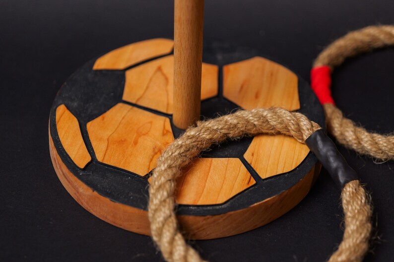Op de afbeelding: Houten ringwerpspel met een voetbalbasis. De basis is gemaakt van hout en zwart en bruin geverfd om op een voetbal te lijken. Het spel bevat twee touwen.