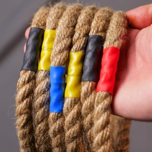 Op de afbeelding: Vijf bruine touwen met gekleurde tape-markeringen. De touwen zijn gebundeld en hebben blauwe, gele, rode en zwarte tape.