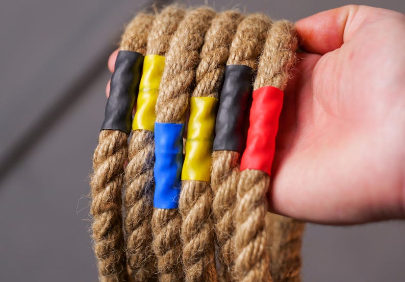 Op de afbeelding: Vijf bruine touwen met gekleurde tape-markeringen. De touwen zijn gebundeld en hebben blauwe, gele, rode en zwarte tape.